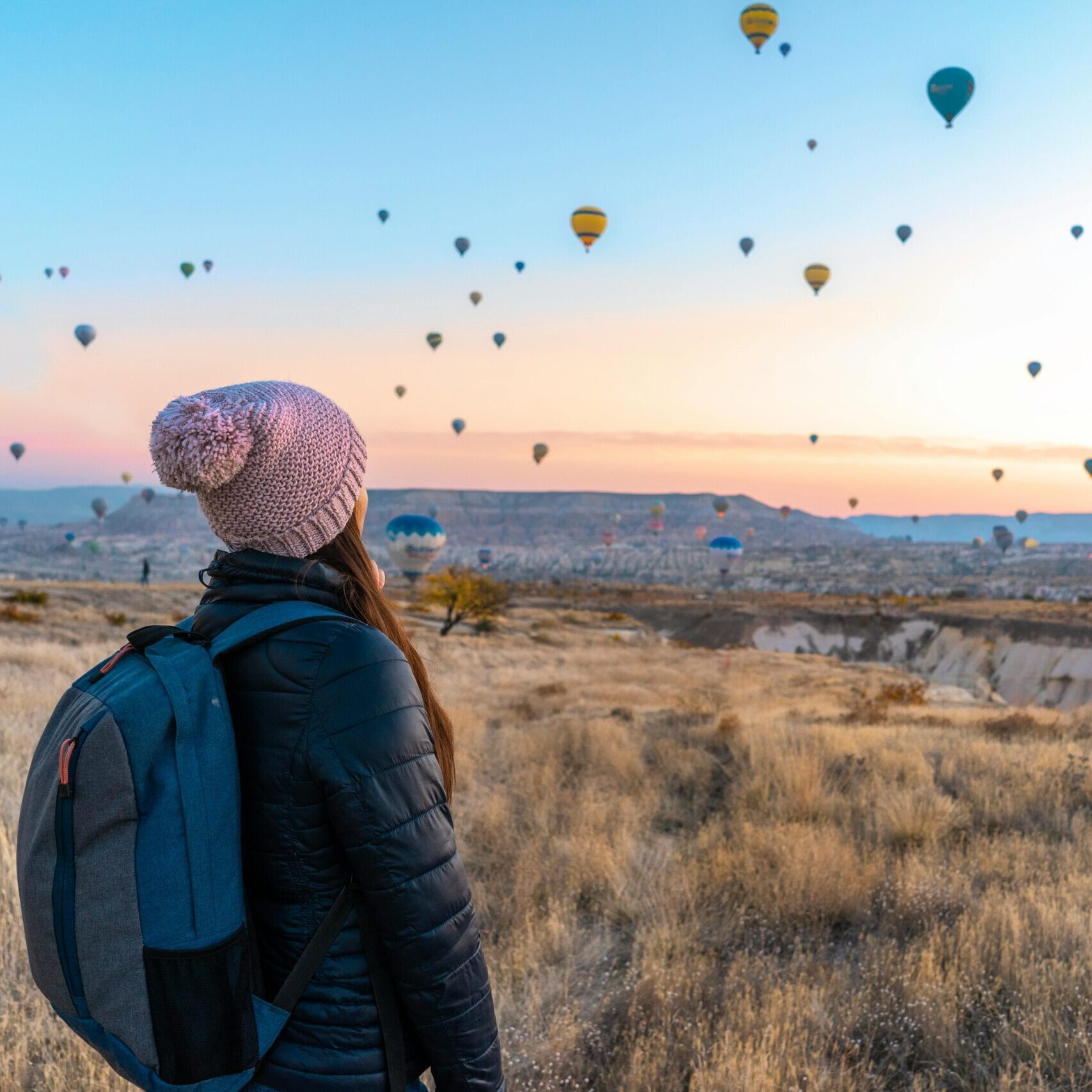 Woman watching hot air balloons in Cappadocia at sunrise, a popular travel destination.