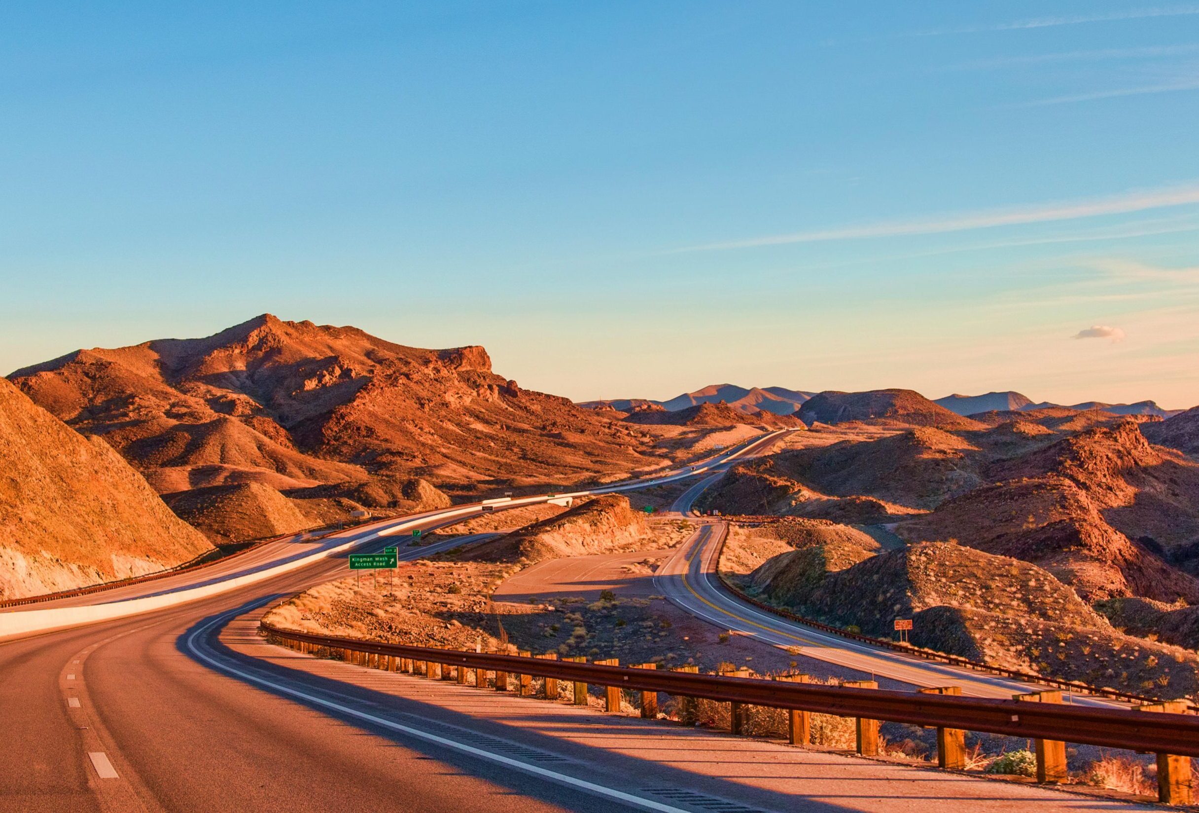 Stunning view of a winding highway amidst Nevada's rugged landscape under blue skies at sunset.